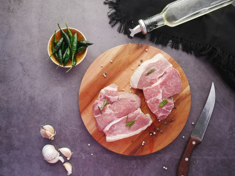 Raw pork collar steaks on a round board
